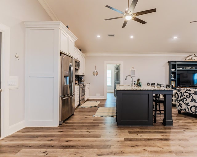 kitchen featuring appliances with stainless steel finishes, a kitchen island with sink, light stone counters, ornamental molding, and white cabinets