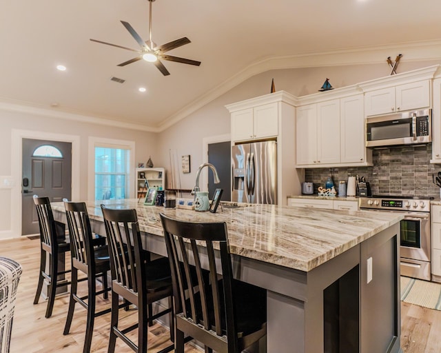 kitchen featuring appliances with stainless steel finishes, white cabinetry, light stone counters, vaulted ceiling, and a large island with sink