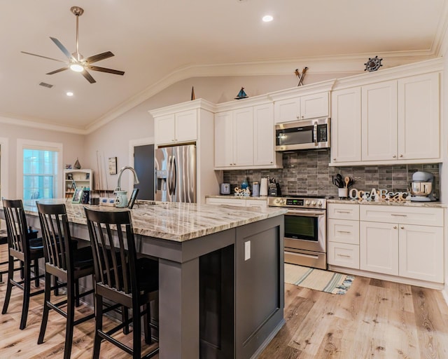 kitchen with light stone countertops, white cabinetry, appliances with stainless steel finishes, and a kitchen island with sink