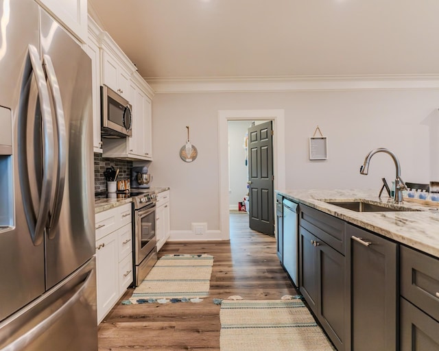 kitchen featuring sink, white cabinetry, light stone counters, ornamental molding, and appliances with stainless steel finishes