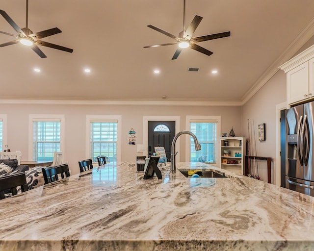 kitchen featuring sink, stainless steel fridge with ice dispenser, ornamental molding, a kitchen breakfast bar, and light stone countertops