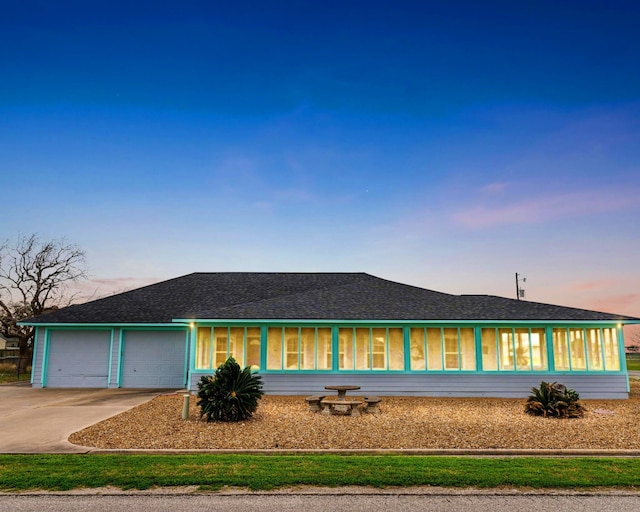 view of front of home with roof with shingles, an attached garage, a sunroom, and driveway