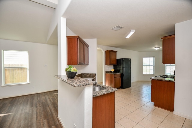 kitchen with light tile patterned flooring, black fridge, dark stone counters, kitchen peninsula, and stainless steel gas stovetop