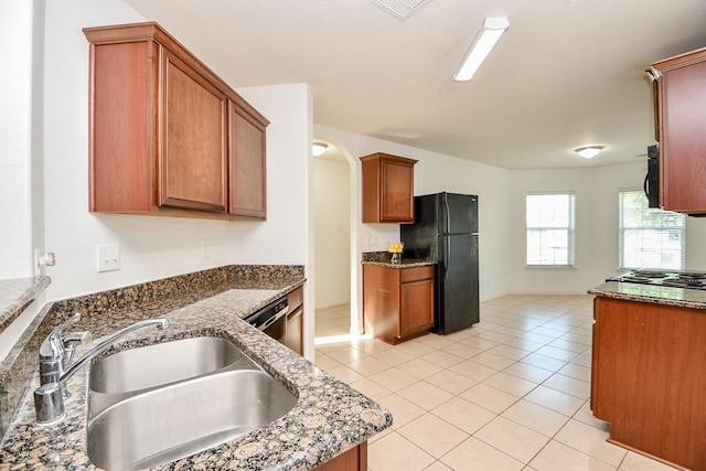 kitchen featuring stainless steel appliances, light tile patterned flooring, sink, and dark stone countertops