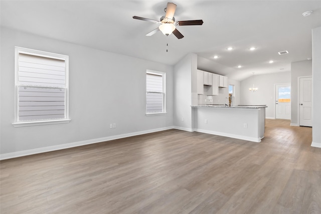 unfurnished living room with vaulted ceiling, ceiling fan with notable chandelier, and light hardwood / wood-style floors