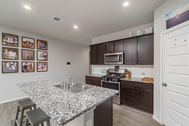 kitchen with dark brown cabinetry, sink, appliances with stainless steel finishes, an island with sink, and decorative backsplash