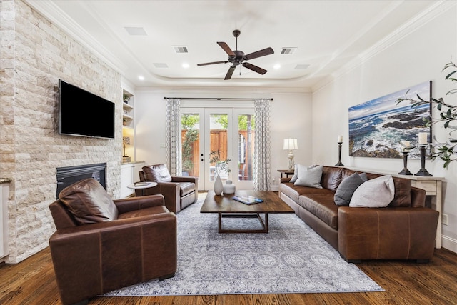 living room featuring visible vents, wood finished floors, a tray ceiling, crown molding, and a stone fireplace