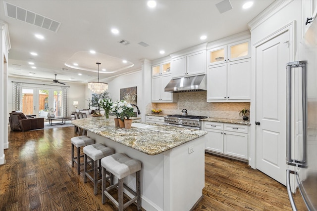 kitchen with a kitchen island with sink, premium appliances, decorative light fixtures, and white cabinets