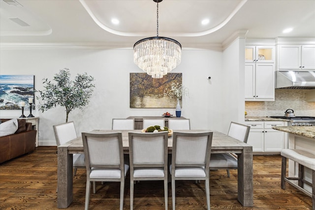 dining area with a notable chandelier, a tray ceiling, dark wood-type flooring, and ornamental molding