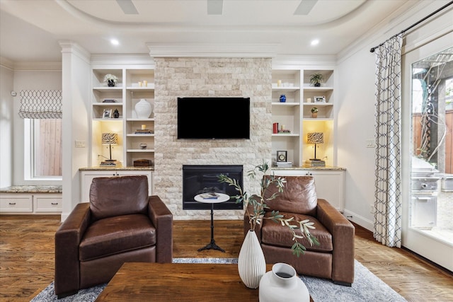 living room featuring wood-type flooring, a stone fireplace, built in features, and crown molding