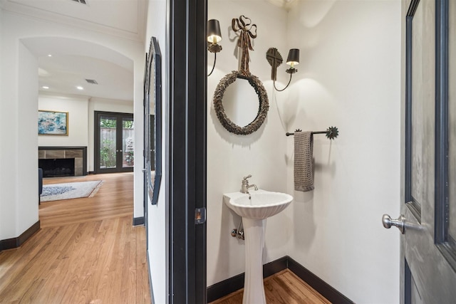 bathroom featuring crown molding, hardwood / wood-style floors, a tile fireplace, and french doors