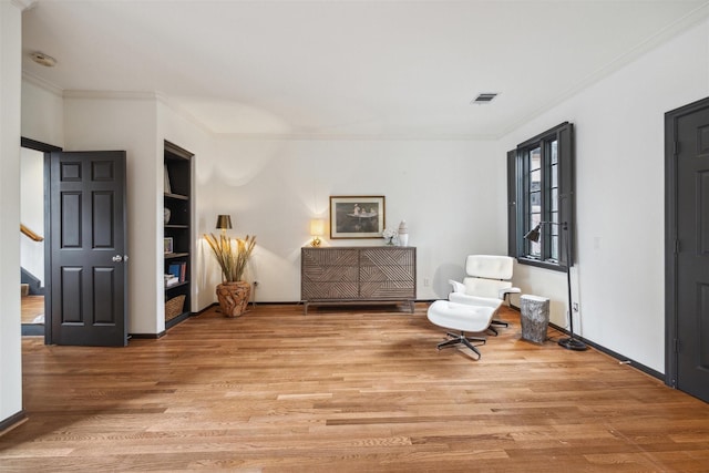 sitting room featuring ornamental molding, built in features, and light hardwood / wood-style floors