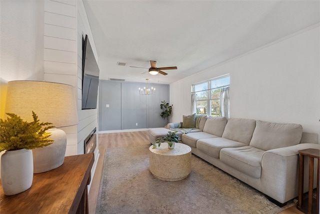 living area featuring a lit fireplace, visible vents, wood finished floors, and ceiling fan with notable chandelier