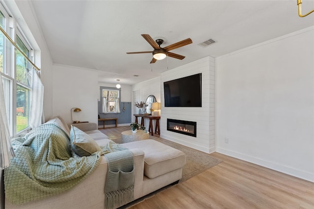 living area with a large fireplace, visible vents, baseboards, and wood finished floors