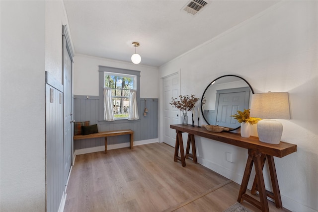 foyer entrance with visible vents, ornamental molding, wood finished floors, and wainscoting