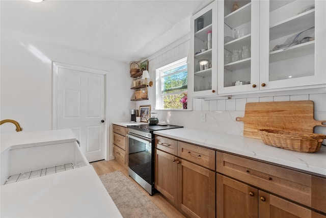 kitchen featuring light stone counters, electric stove, brown cabinets, light wood-style flooring, and glass insert cabinets