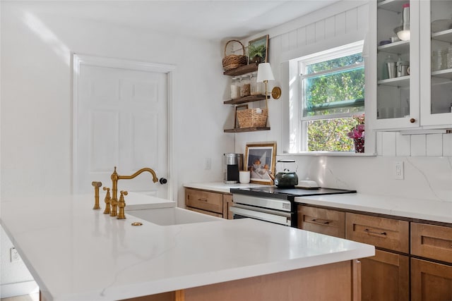 kitchen with decorative backsplash, brown cabinets, stainless steel range with electric cooktop, open shelves, and a sink