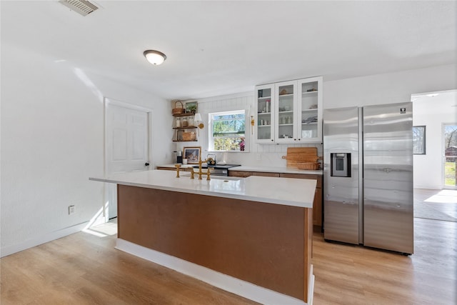 kitchen featuring visible vents, light countertops, light wood-type flooring, stainless steel fridge with ice dispenser, and glass insert cabinets