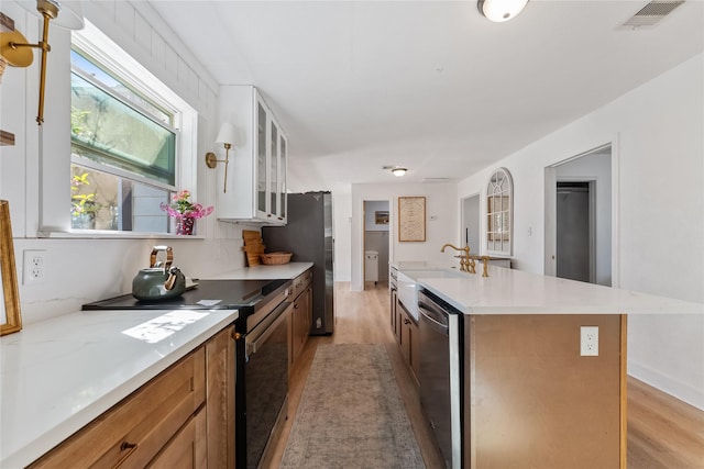 kitchen featuring light wood finished floors, light countertops, visible vents, appliances with stainless steel finishes, and glass insert cabinets