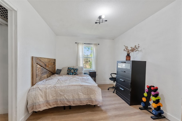 bedroom with a textured ceiling, light wood-type flooring, and baseboards