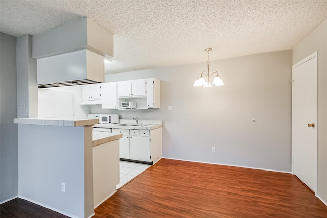 kitchen featuring white cabinetry, kitchen peninsula, light wood-type flooring, and decorative light fixtures