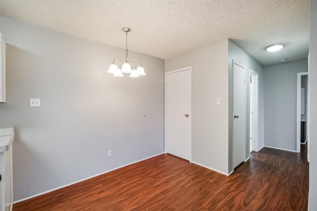 unfurnished dining area featuring a textured ceiling, a notable chandelier, and dark hardwood / wood-style flooring