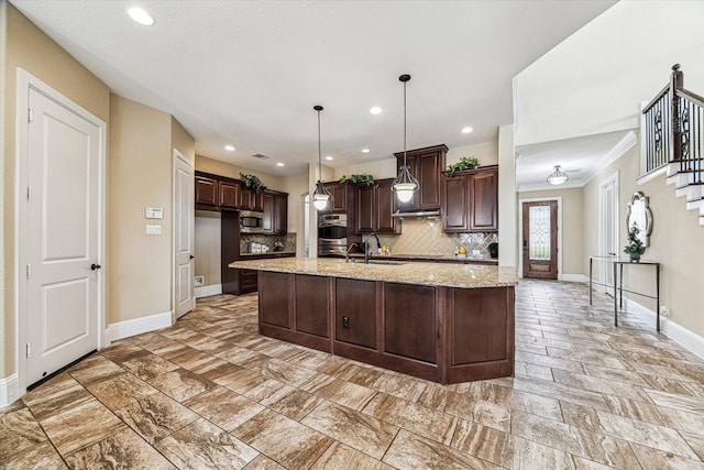 kitchen featuring sink, hanging light fixtures, light stone counters, dark brown cabinets, and a center island with sink