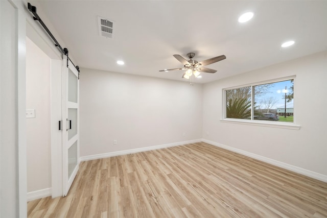 unfurnished bedroom featuring ceiling fan, a barn door, and light wood-type flooring