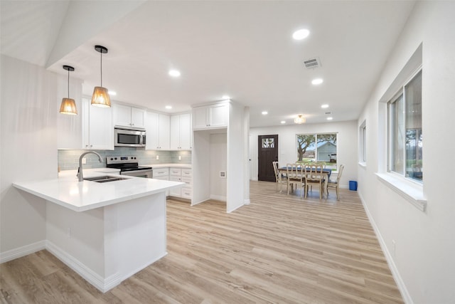 kitchen featuring sink, hanging light fixtures, kitchen peninsula, stainless steel appliances, and white cabinets