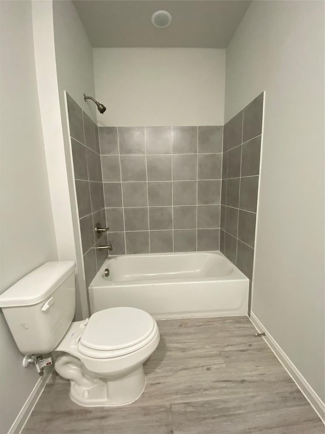 bathroom with wood-type flooring, tiled shower / bath, and toilet