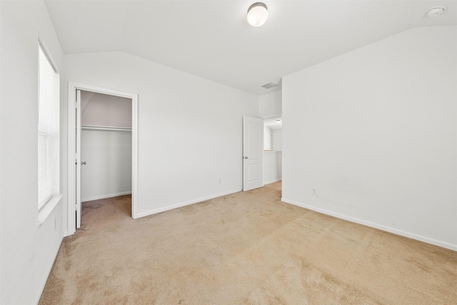 unfurnished bedroom with a walk in closet, lofted ceiling, light colored carpet, and a closet