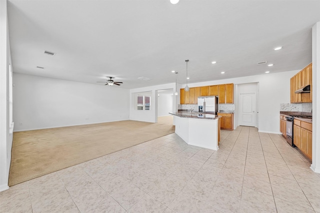 kitchen featuring backsplash, hanging light fixtures, stainless steel appliances, a center island with sink, and light carpet