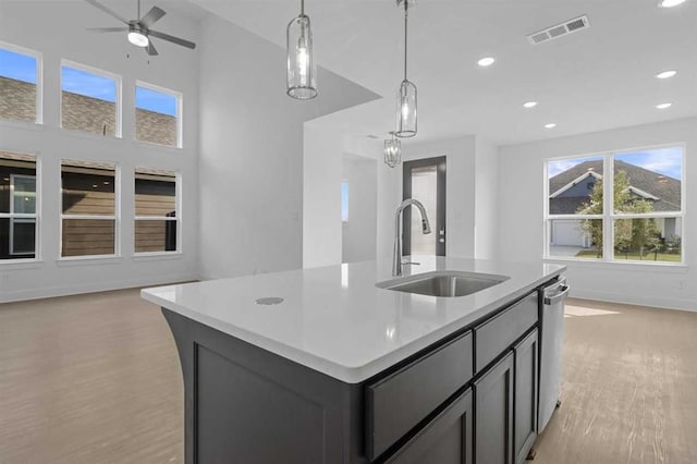 kitchen featuring sink, light hardwood / wood-style floors, an island with sink, decorative light fixtures, and stainless steel dishwasher