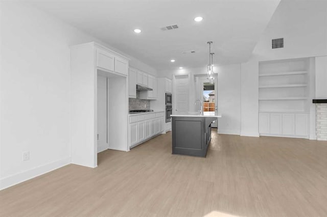 kitchen featuring white cabinetry, gas stovetop, decorative light fixtures, and an island with sink