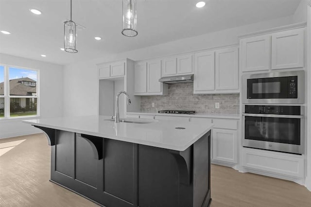 kitchen featuring a center island with sink, white cabinetry, pendant lighting, and stainless steel oven