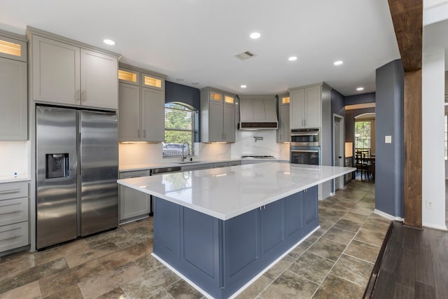 kitchen with gray cabinets, premium range hood, sink, stainless steel appliances, and a spacious island