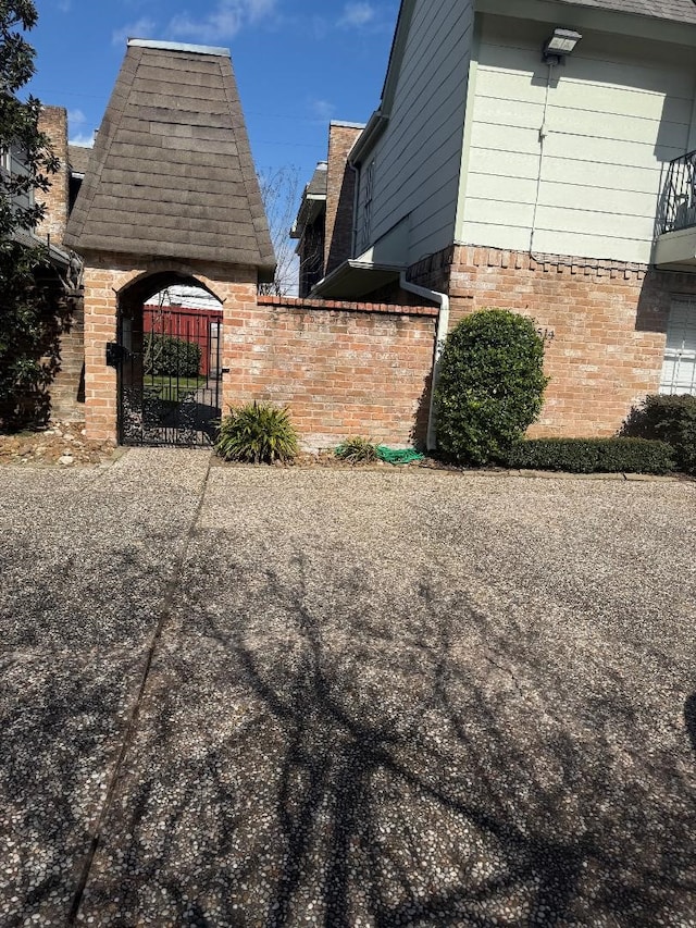 view of home's exterior with a shingled roof, a gate, and brick siding