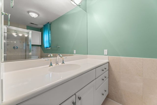 bathroom with a stall shower, vanity, visible vents, and tile walls