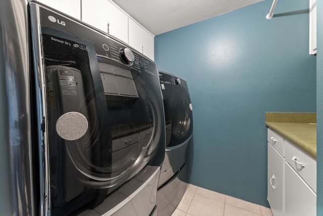 clothes washing area with a textured ceiling, light tile patterned flooring, cabinet space, and washer and dryer