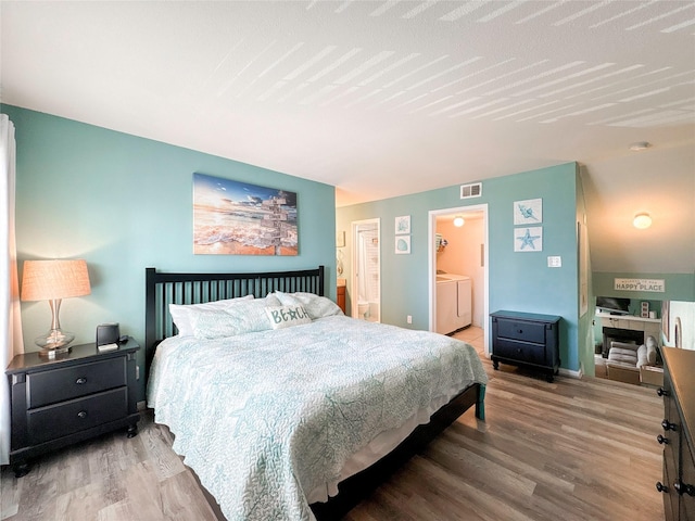 bedroom featuring hardwood / wood-style floors, washer / dryer, and ensuite bath