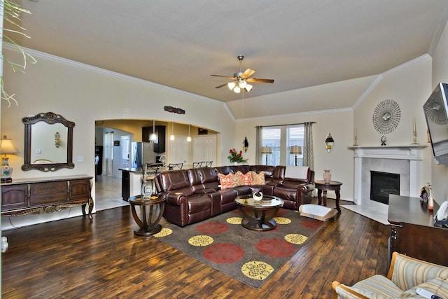 living room with vaulted ceiling, a fireplace, wood-type flooring, ornamental molding, and ceiling fan