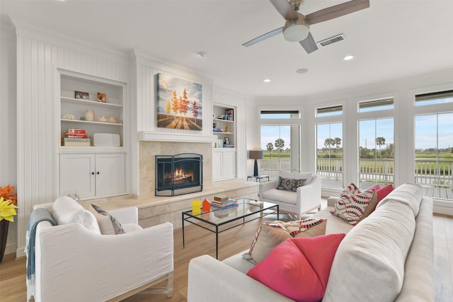 living room with crown molding, built in features, a high end fireplace, and light hardwood / wood-style floors