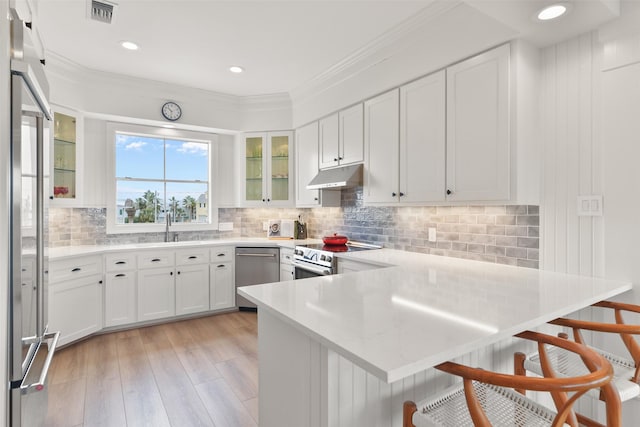 kitchen with appliances with stainless steel finishes, white cabinets, a kitchen bar, kitchen peninsula, and crown molding