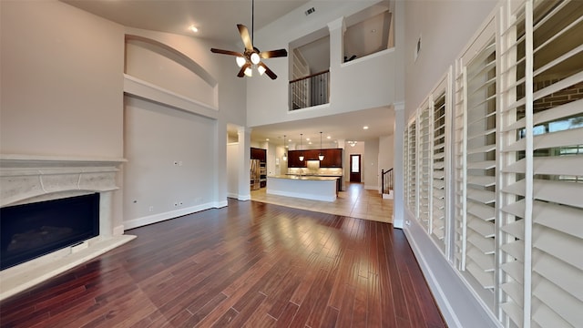 unfurnished living room featuring baseboards, visible vents, a fireplace with raised hearth, a ceiling fan, and dark wood-style floors