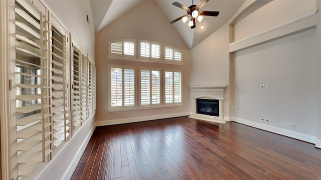 unfurnished living room with dark wood-style floors, a glass covered fireplace, ceiling fan, high vaulted ceiling, and baseboards