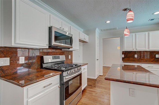 kitchen featuring dark stone countertops, appliances with stainless steel finishes, decorative light fixtures, and white cabinets