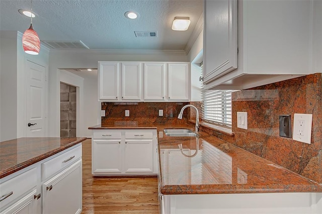 kitchen featuring pendant lighting, white cabinetry, sink, dark stone counters, and light hardwood / wood-style flooring