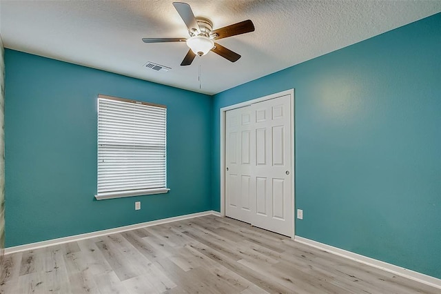 unfurnished bedroom with ceiling fan, a closet, a textured ceiling, and light wood-type flooring