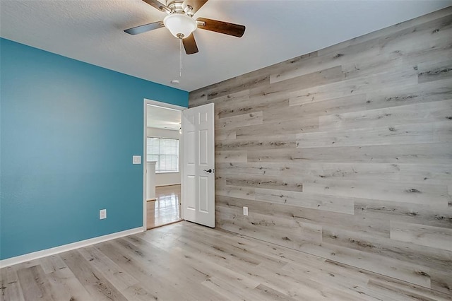 unfurnished room with light hardwood / wood-style flooring, ceiling fan, and wood walls