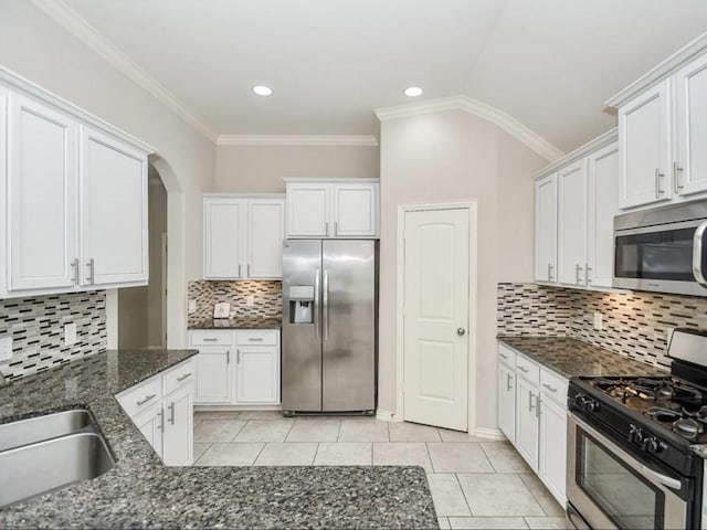 kitchen with light tile patterned floors, crown molding, appliances with stainless steel finishes, white cabinetry, and dark stone counters